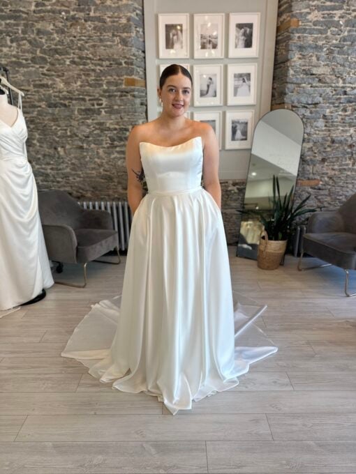 Ginni, a light satin aline wedding dress with a leg slit and pockets. A cat eye neckline and detachable sleeves.