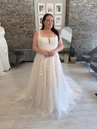 plus size bride standing in a lace a line wedding dress with a notched neckline